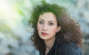 Portrait of the woman with make-up and curly hair, at blurred background, in light