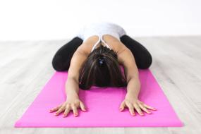 Woman doing child's pose stretch on pink mat