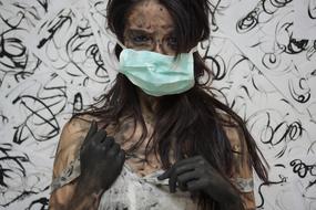 Portrait of the woman in dirt, with the mask and gloves, near the wall, with the black drawings