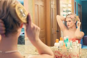 blonde combing her hair in front of a mirror with doors on the background