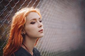 Portrait of the beautiful girl with ginger hair and piercings, near the wire mesh