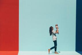 a woman holds a baby in her arms against a background of a multicolored striped wall