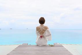 young woman in white dress sits in front of tranquil sea