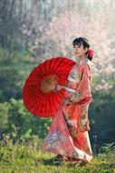 Beautiful woman in colorful kimono, with the umbrella, on the green mountain in Japan