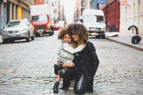 Cute mom and daughter with curly hair, on the road, among the buildings and cars