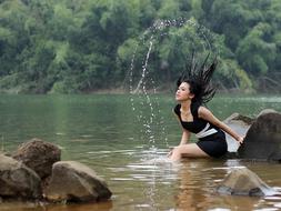 Wet girl in black and white dress, sitting on the rock, among the water