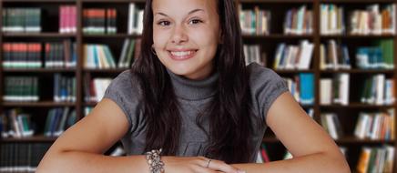 smiling attractive girl sits in front of Books on shelves