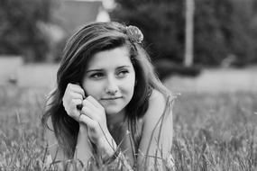 Black and white portrait of a girl with a flower on the head, laying on the grass
