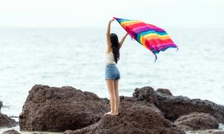 photo of a girl on the seashore with a rainbow scarf in her hands