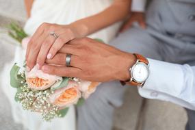 Hands of the bride and groom with rings, on the colorful and beautiful flowers