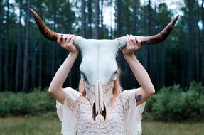 woman holds animal Skull with long Horns in front of head