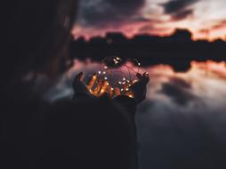 Beautiful lights in the hands of a woman, near the beautiful water, with the reflections of the trees and colorful sunset