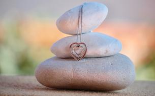 female pendant in the shape of a heart on stones close-up on blurred background