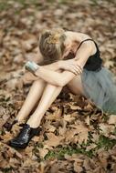 sad girl is sitting on autumn foliage