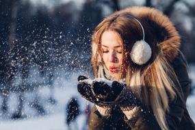 photo of a girl blowing on snowflakes in the winter forest