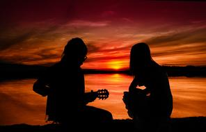 man with guitar and girl, silhouettes at Sunset sky