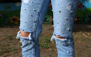female legs in blue Jeans Pants with pearls and holes in knees