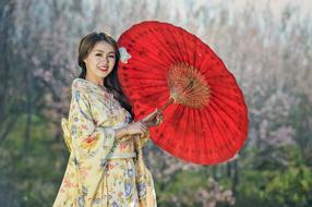 happy young asian woman in kimono posing with traditional red umbrella
