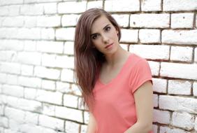 Portrait of the woman in pink t-shirt, posing near the white brick wall