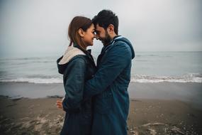 Side view of the couple, together, on the beautiful sandy beach, under the cloudy sky