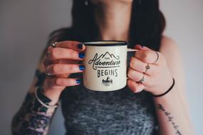 Woman with tattoos and blue nail polish, drinking from the white and black mug