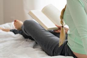 girl sits with book on Bed