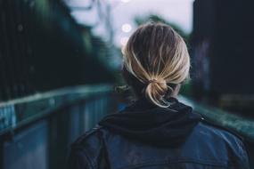 Back view of a blonde girl in black leather jacket, near the bridge