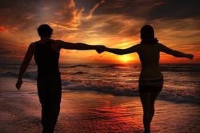 couple in love walks along the beach against the backdrop of a colorful sunset