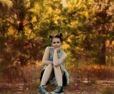 Posing girl, sitting on the colorful and beautiful field, among the trees