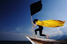 woman wearing Yellow Cape standing on boat with black flag, collage