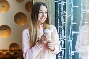 girl with a glass of coffee stands at the window in a cafe