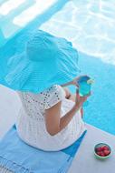girl in a blue hat with a cocktail sitting by the pool