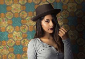 Portrait of the beautiful girl, with the shiny skin, make-up and hat, near the colorful, patterned wall