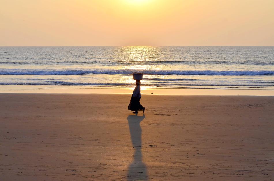 a woman walks along the beach near the sea in India