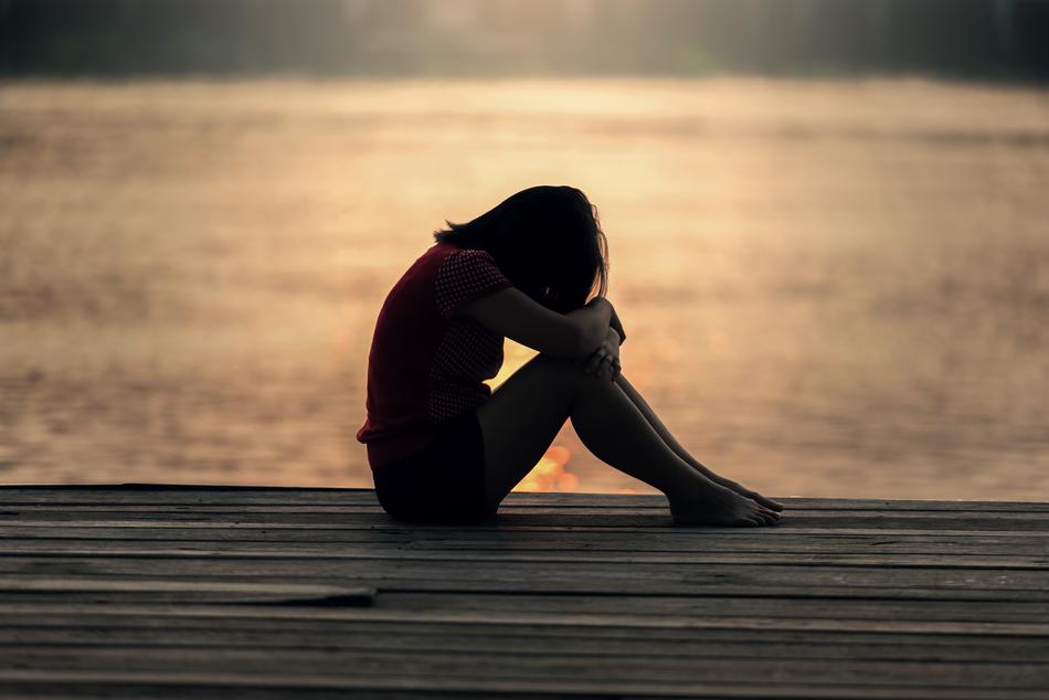 sad girl sitting on the pier in the evening