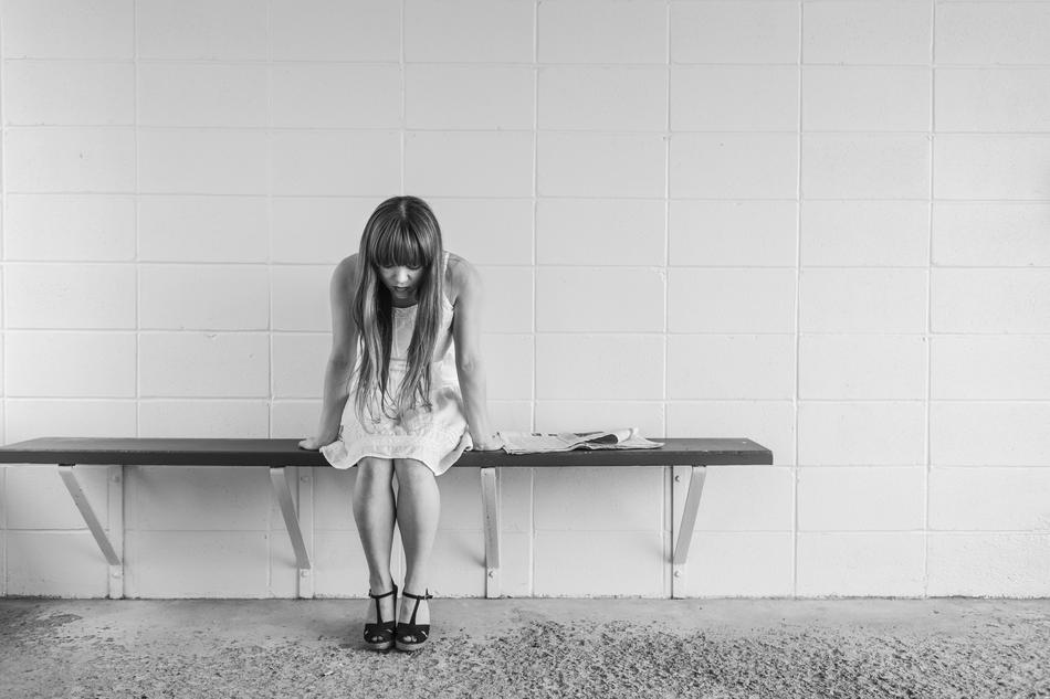 worried girl sitting on a bench against a background of a hospital wall