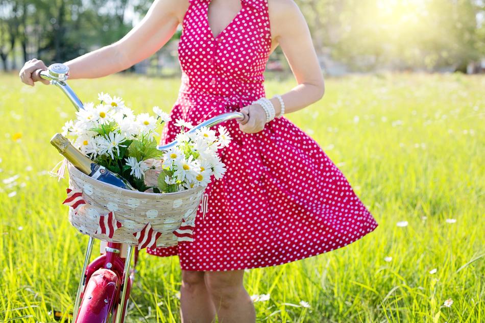 Woman in red Dress with Bicycle on meadow at summer