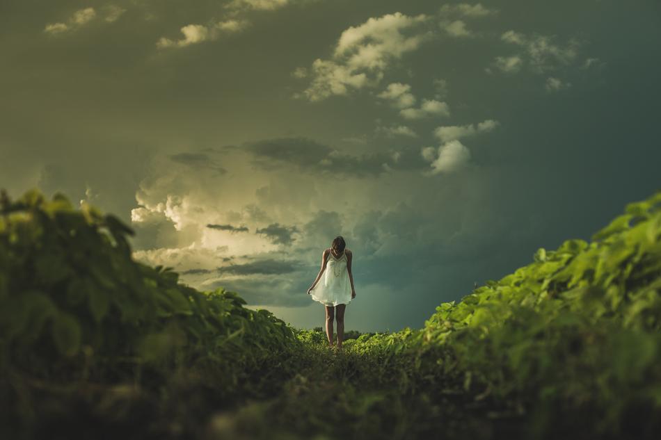 Girl in white dress, on the beautiful green hills, under the cloudy sky in summer