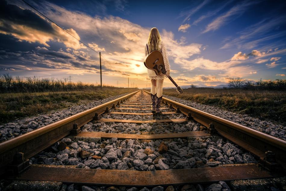 a girl with a guitar walks along the railroad tracks