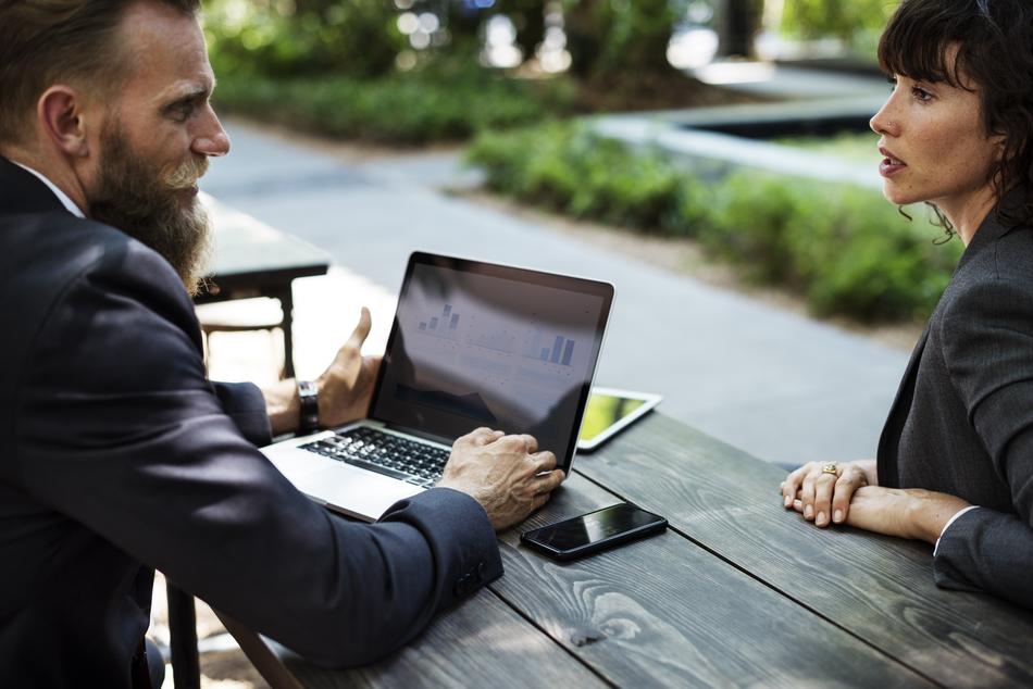 Bearded man in suit, using the laptop, near the woman in suit