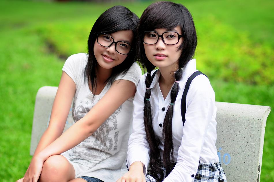 Portrait of the two, Asian girls on the bench, near the green grass