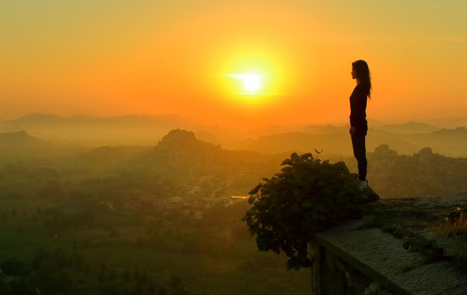 Silhouette of a girl, standing on the beautiful mountain, at colorful sunrise in Hampi, India