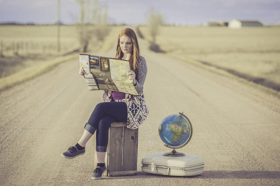 photo of a girl sitting on a suitcase with a map on the highway