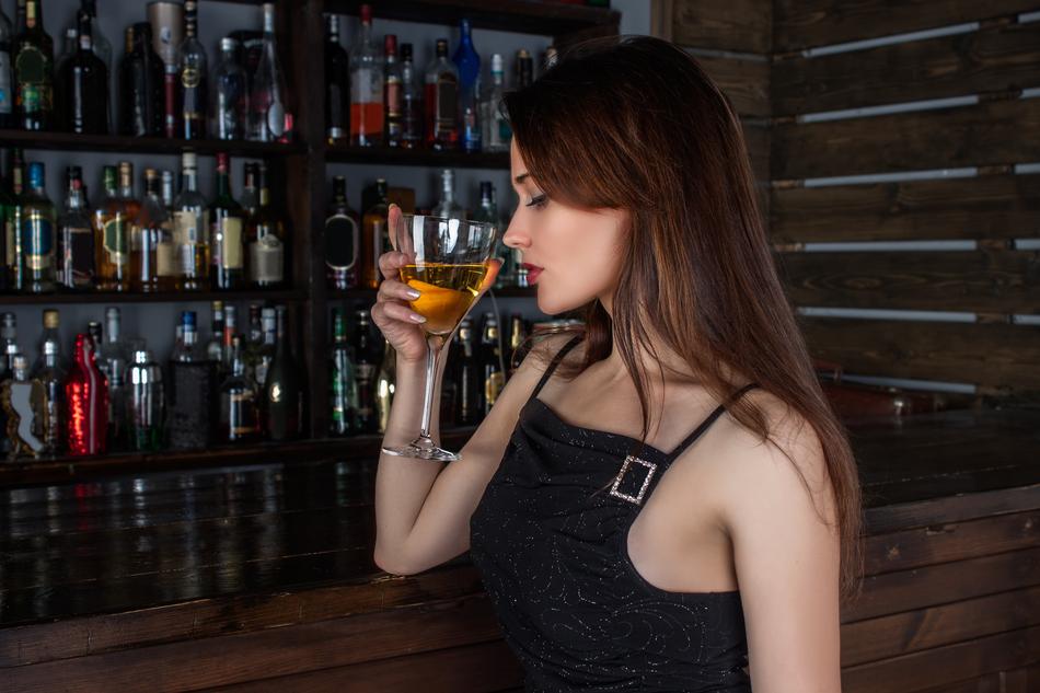 Profile portrait of the woman with the alcohol drink, near the bar