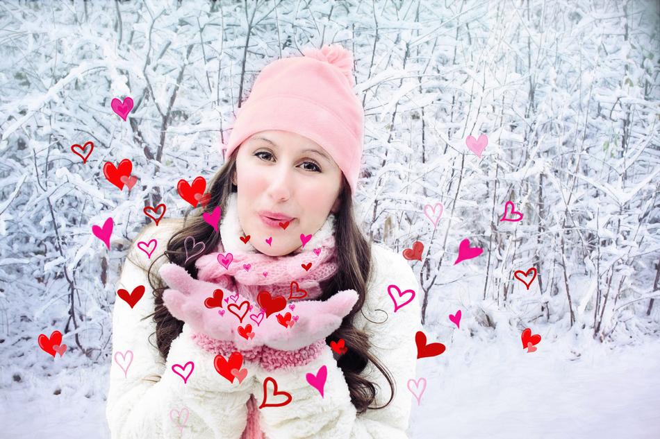Portrait of the woman blowing kisses, with the hearts, among the beautiful, snowy trees in winter