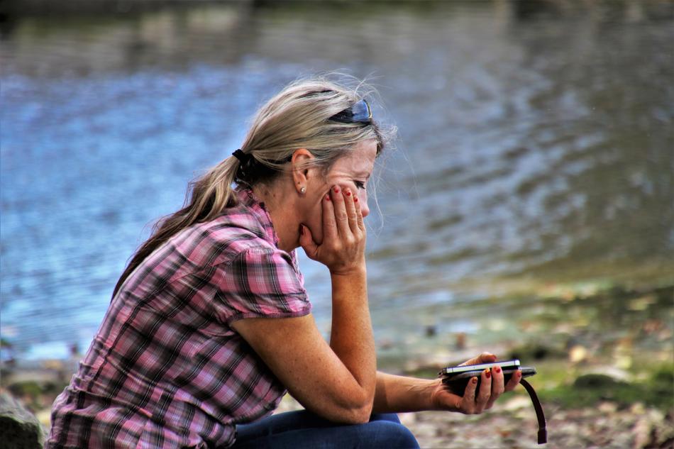 pensive woman with smartphones in hands by the lake