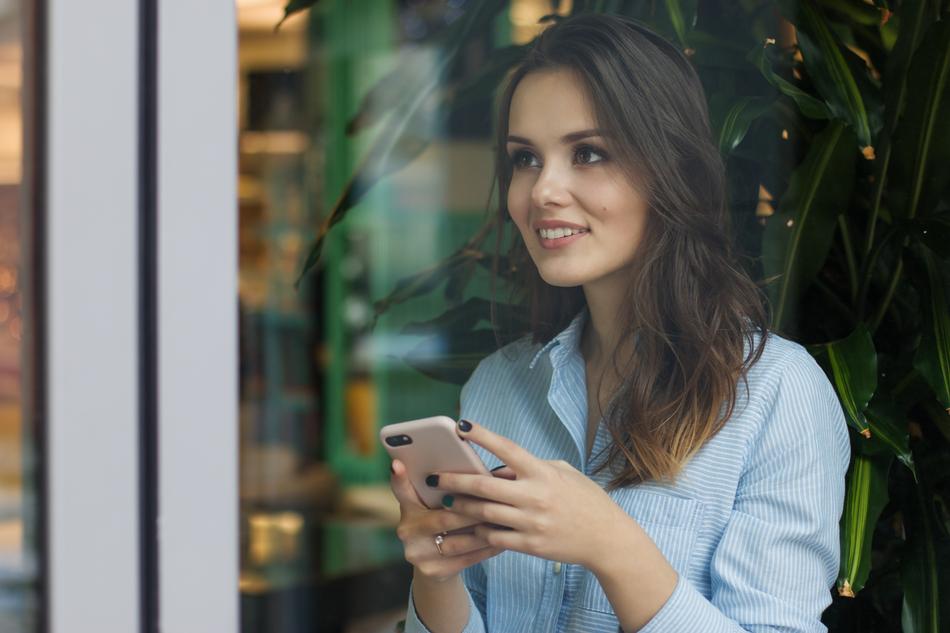 photo through the glass of a smiling girl with a smartphone