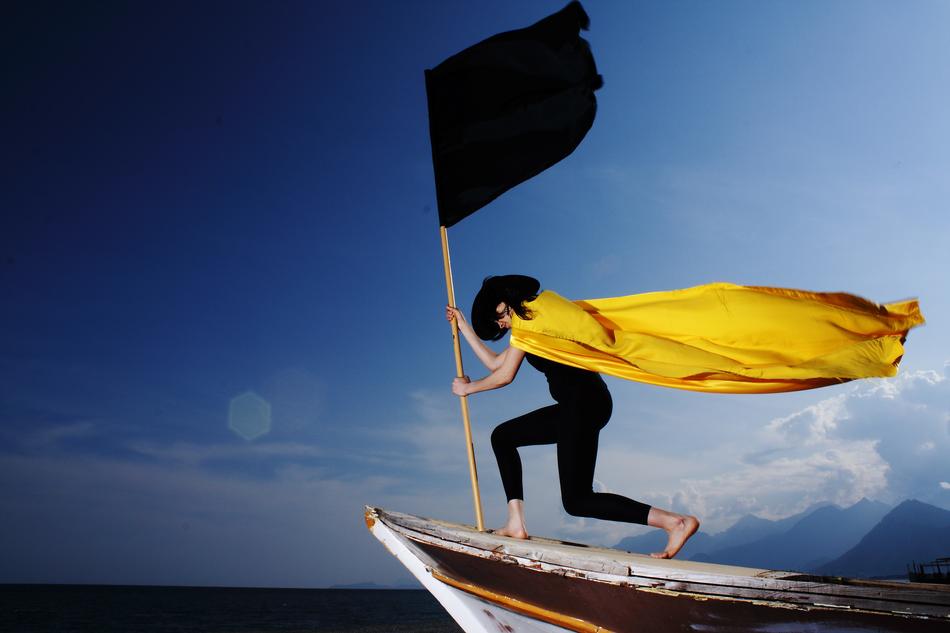 woman wearing Yellow Cape standing on boat with black flag, collage