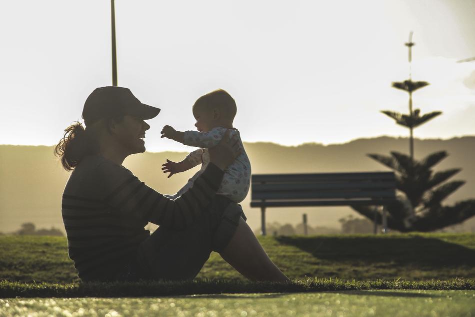 Mother with the child on the beautiful green field with tree and bench, near the mountains, in sunlight