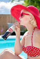 Woman in red hat drinks coca-cola at Pool